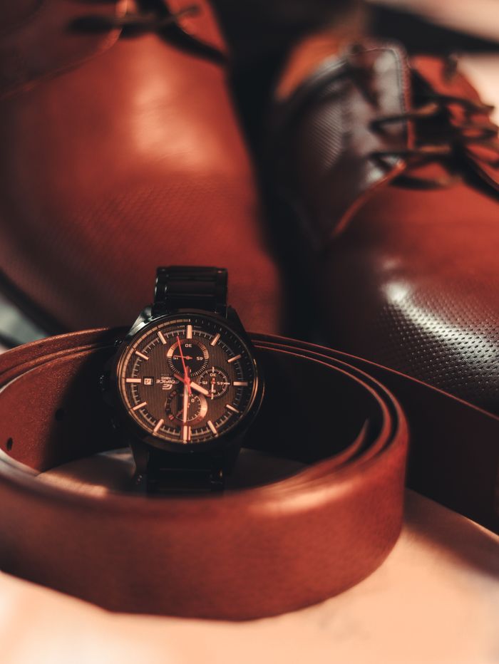 about-us Close-up of a stylish men's wristwatch with leather shoes and belt, highlighting elegance and fashion.