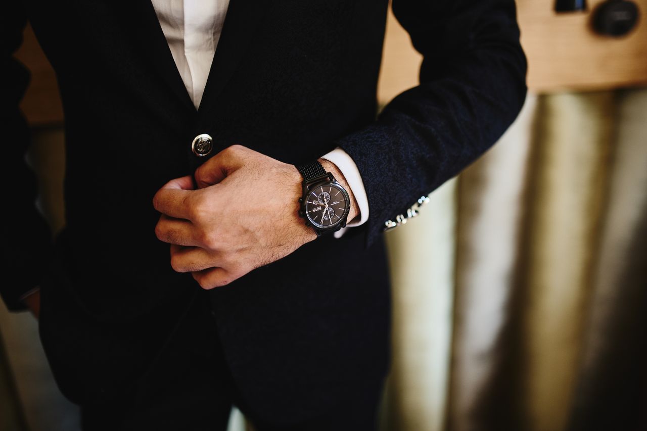 heros-img Close-up of a man in a black suit, showcasing a stylish wristwatch. Perfect for fashion and business themes.